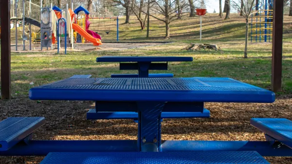 Blue picnic table with attached benches and colorful children's playground in background.