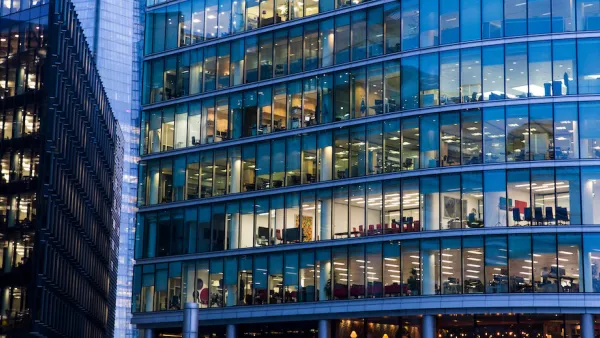 Close-up of glass facade of office building with office furniture visible through the windows.