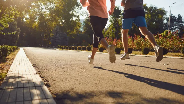Two people run down a paved path in the city, surrounded by landscaping.