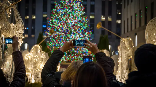 Tourists holding up cameraphones taking photos of Rockefeller Center Christmas tree in New York City.