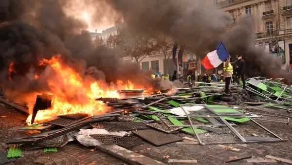 Person stands next to pile of burning debris in street holding French flag during Yellow Vest protests