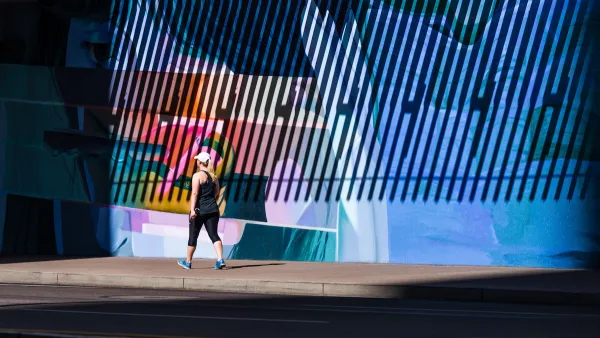 Woman in exercise clothes walking on sidewalk against large wall with mural in Phoenix, Arizona.