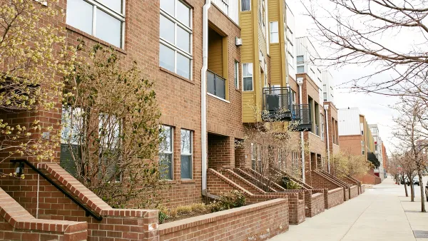Row of light red brick condominium buildings along quiet street with concrete sidewalk in Denver, Colorado.