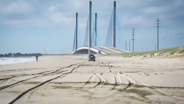 View of sand dunes with one truck and one fisherman at seashore in Delaware with Indian River Inlet Bridge in background.