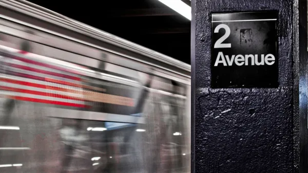 Close-up of 2 Avenue sign on column in NYC subway station with train passing by in background.