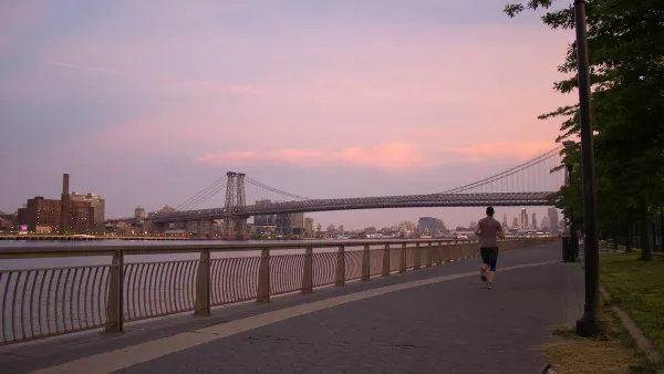 Sunset view of Williamsburg Bridge from East River Park walkway next to river with one jogger.