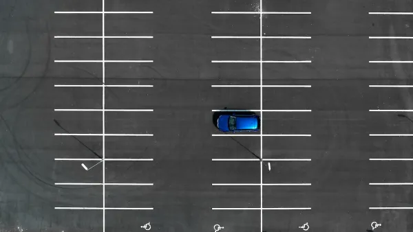 Bird's eye view of empty asphalt parking lot with one blue car.