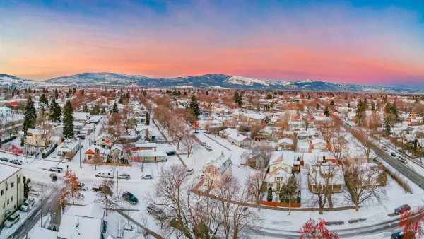Large homes in neighborhood covered in snow in Missoula, Montana with mountains in background gainst sunset sky.
