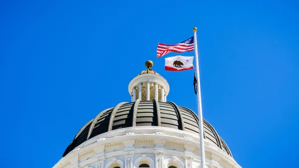 Close-up of top of California state capitol dome with U.S. and California flags flying and blue sky in background.