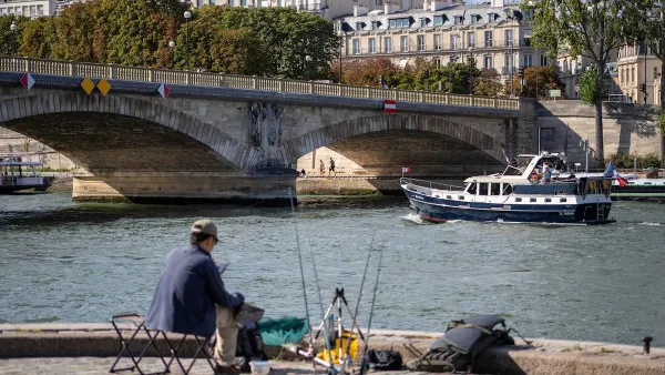 Man sitting in chair along River Seine in Paris with fishing pole.
