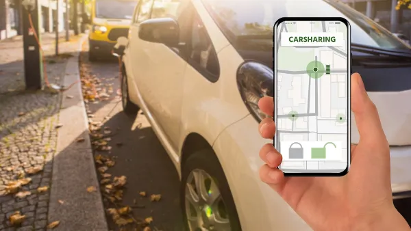 Close-up of hand holding up phone with car sharing app open in front of parked cars.