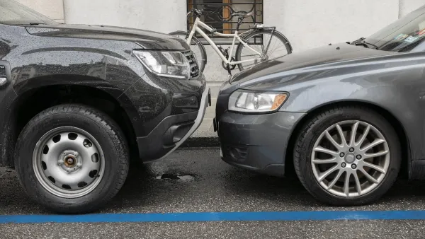 Two grey cars parked nose to nose, one taller than the other, on city curb with parked bicycle visible on sidewalk.