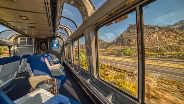 View from inside glass top floor of Amtrak passenger train with Rocky Mountains scenery outside.