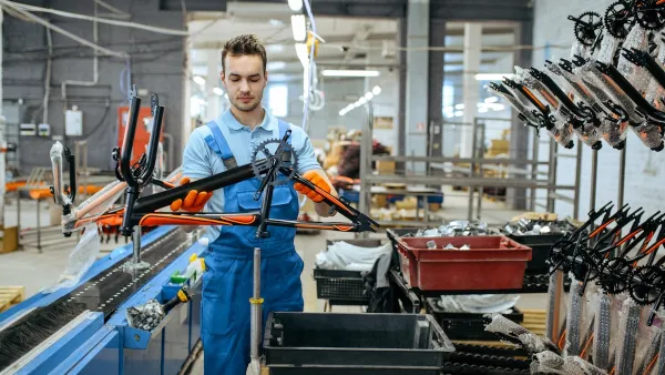 Worker in bicycle factory holding black and orange bike frame.