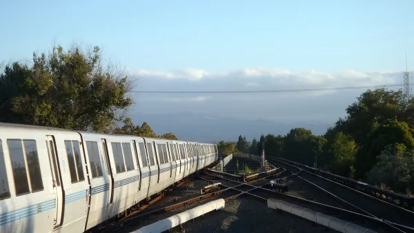 BART heavy rail train on elevated track pulling into Concord, CA station with cloudy sky and trees in background.