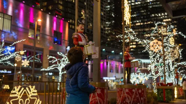 Child looking up at Christmas lights in city at night.