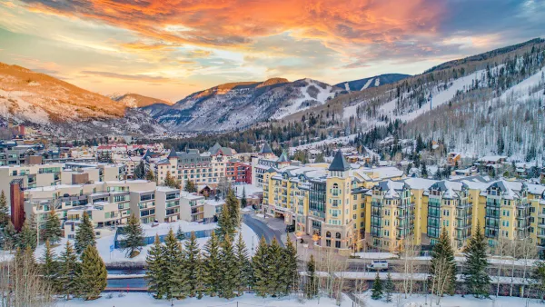 Aerial view of Vail, Colorado in winter with multi-story buildings in foregorund and snowy mountains in background.
