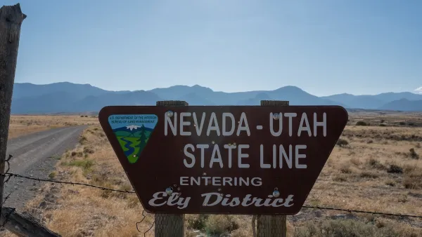 Roadside sign for Nevada Utah State Line "Entering Ely District" with Bureau of Land Management logo with desert mountains in background.