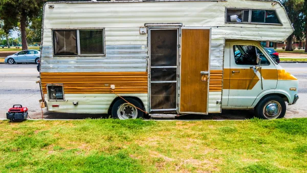 Old white motor home with brown stripe and open door parked on street in Los Angeles, California.