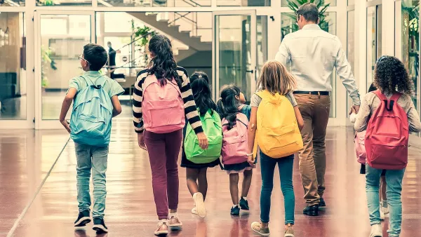 Back view of group of six children and one adult walking down school hallway.