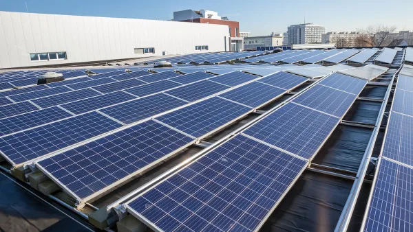 Rows of solar panels on a large rooftop with office or industrial buildings in background.