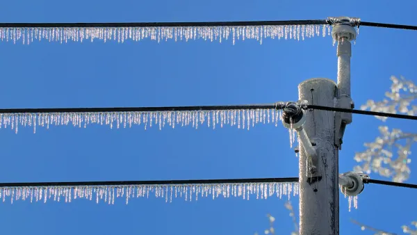 Power lines with dense icicles hanging from them against blue sky.