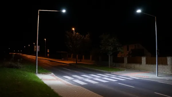 Empty street with crosswalk lit by two tall street lights at night.