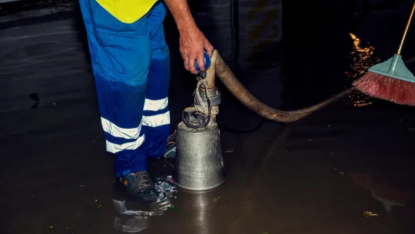 Worker in blue pants holding hose while standing in flooded interior room.