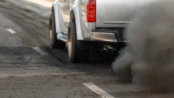 Close-up of driver's side of silver truck with cloud of dirty emissions from tailpipe.