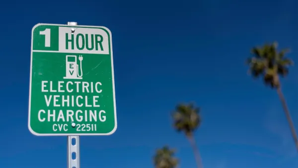 Close-up of green and white sign for 1 hour EV charging station outdoors with tall palm trees in background against blue sky.