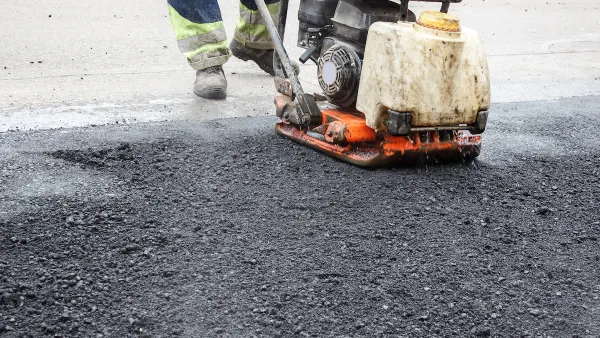 Close-up of worker using machine to press down fresh asphalt on road.