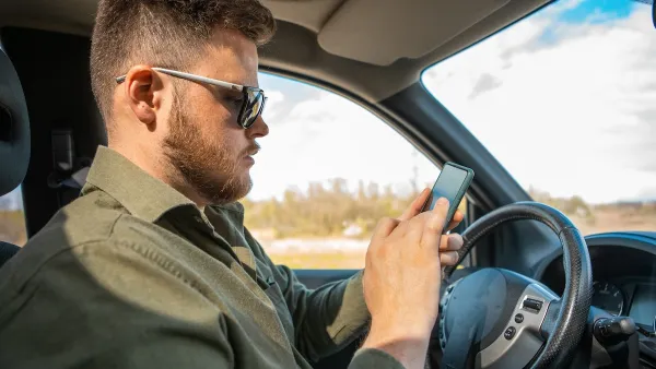 Man sitting in driver's seat looking at cell phone.