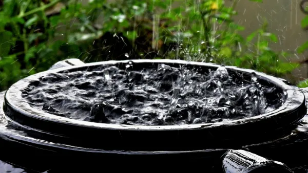 Close-up of top of black rain barrel full of water with raindrops falling on surface.