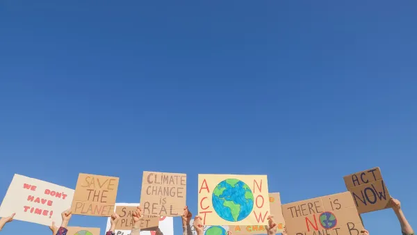 Hands holding up climate change protest signs against blue sky.