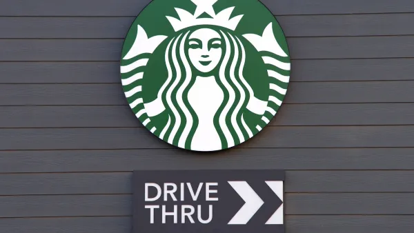 Close-up of Starbucks coffee logo with Drive Thru sign with arrow under it mounted on dark grey wall.