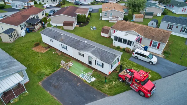 Aerial view of manufactured home being dropped off or moved by red truck in mobile home park