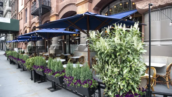 Outdoor dining patio with tables and boxes of flowers surrounding it on New York City sidewalk.