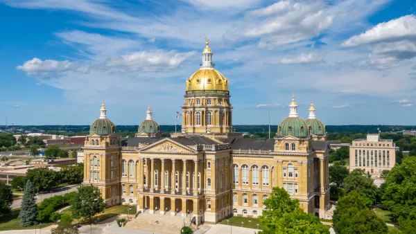 Ornate, tan stone capitol building with a gold dome roof and low-rise city buildings in the background.
