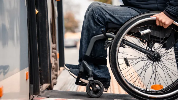 Close-up of person in wheelchair wearing jeans entering public bus on ramp.