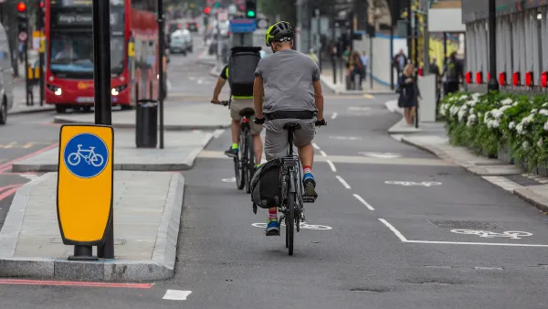 Protected two-way cycletrack on street in London, UK with red double-decker bus in background.