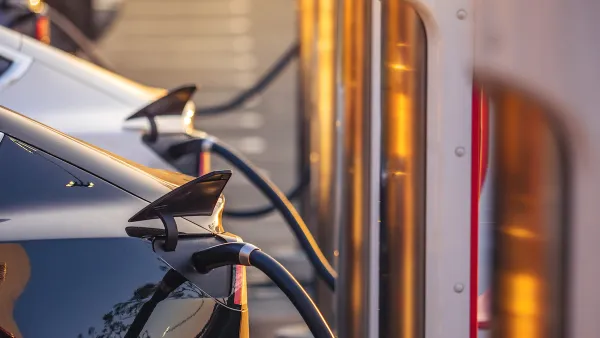 Close-up of row of electric cars plugged into chargers at outdoor station.