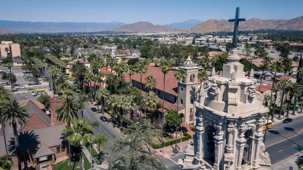 Aerial view of Riverside, California with ornate Catholic church tower in foreground and mountains in the distance.