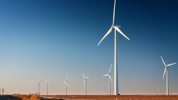 Row of white wind turbines in wide open dirt field in west Texas.