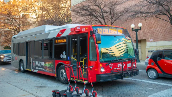 Red public bus on street in San Antonio, Texas with line of four red e-scooters on sidewalk.