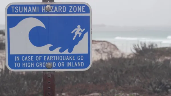 Close-up of blue and white tsunami warning sign on coast in Monterey, California on gloomy day.