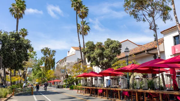 View of Santa Barbara, California street with neo-Spanish colonial architecture and wooden outdoor dining deck with tables and red umbrellas.
