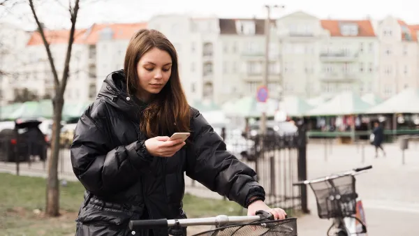 Woman stands next to a bike with one hand on handlebar holding her mobile phone.