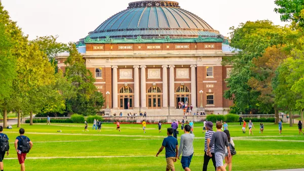 College students walking on green lawn with neoclassical red brick domed building in background on University of Illinois campus.