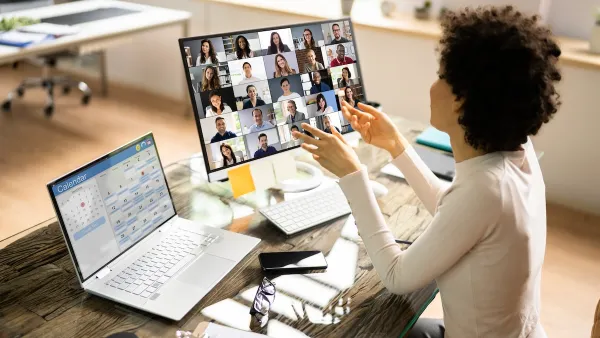 Woman at desk with laptop and extra monitor with Zoom session open.