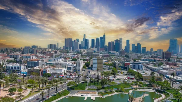 Aerial view of Macarthur Park lake with downtown Los Angeles skyline in background.